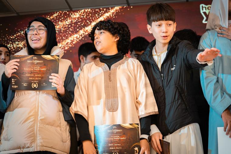 Award recipients holding certificates on stage with a trophy.